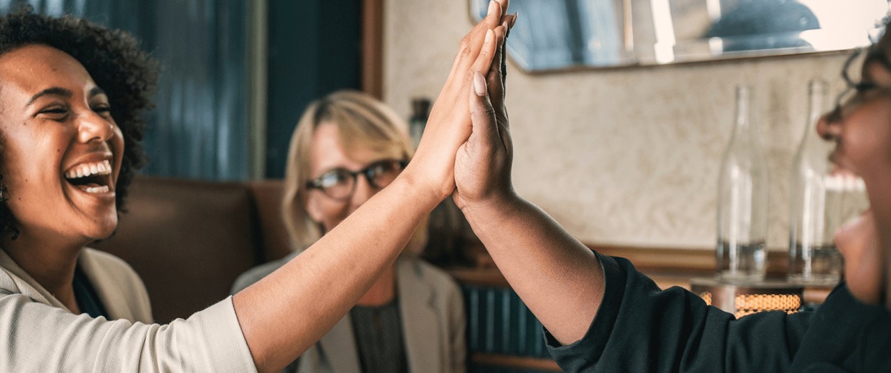 two women high-fiving and one smiling in the background.