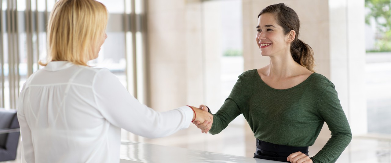 Two women shaking hands at a bright counter.